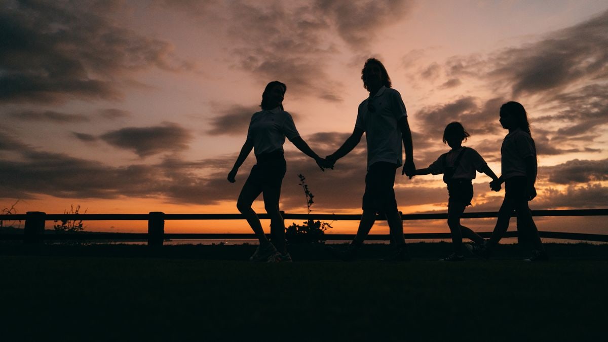 A family walks hand in hand against a vibrant sunset, evoking togetherness and peace.